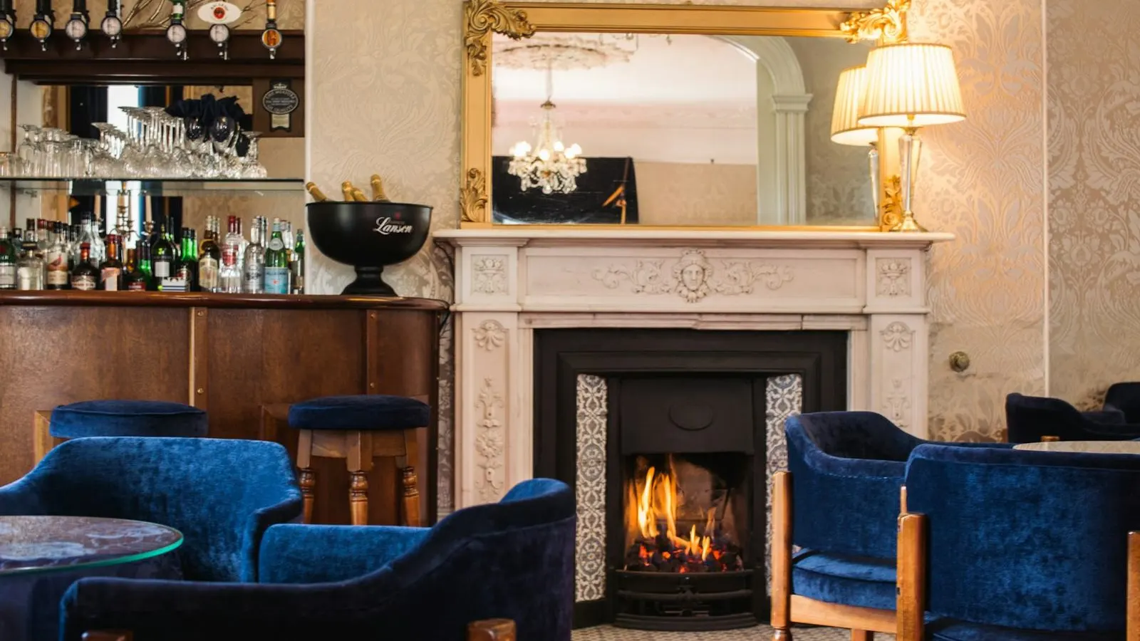 Hotel bar with a fireplace, blue velvet chairs and a gilt mirror