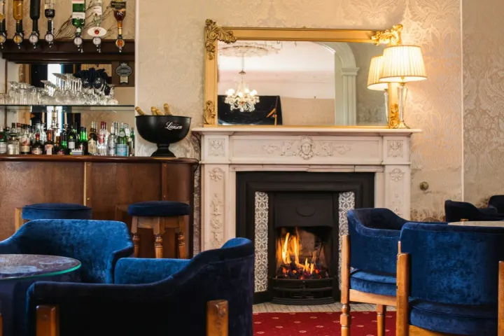 Hotel bar with a fireplace, blue velvet chairs and a gilt mirror