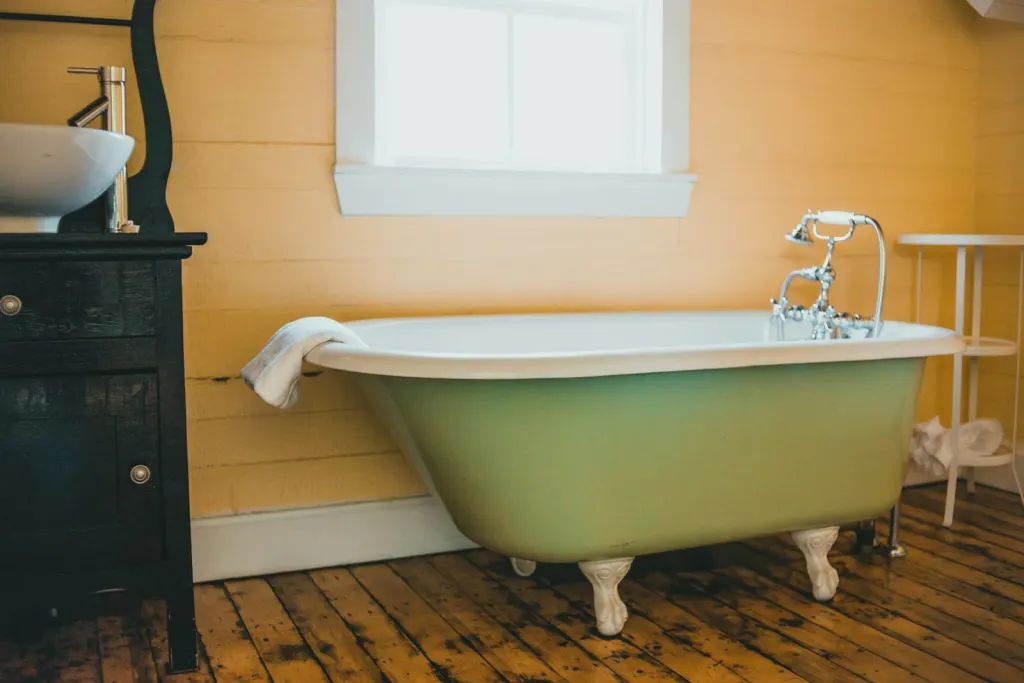 Green roll-top bath on a wooden floor under a small window