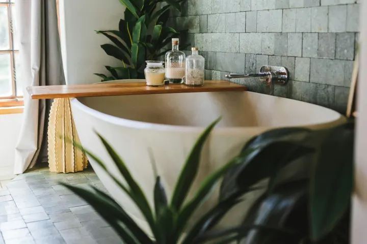 Freestanding stone bath with a plant and a wooden tray