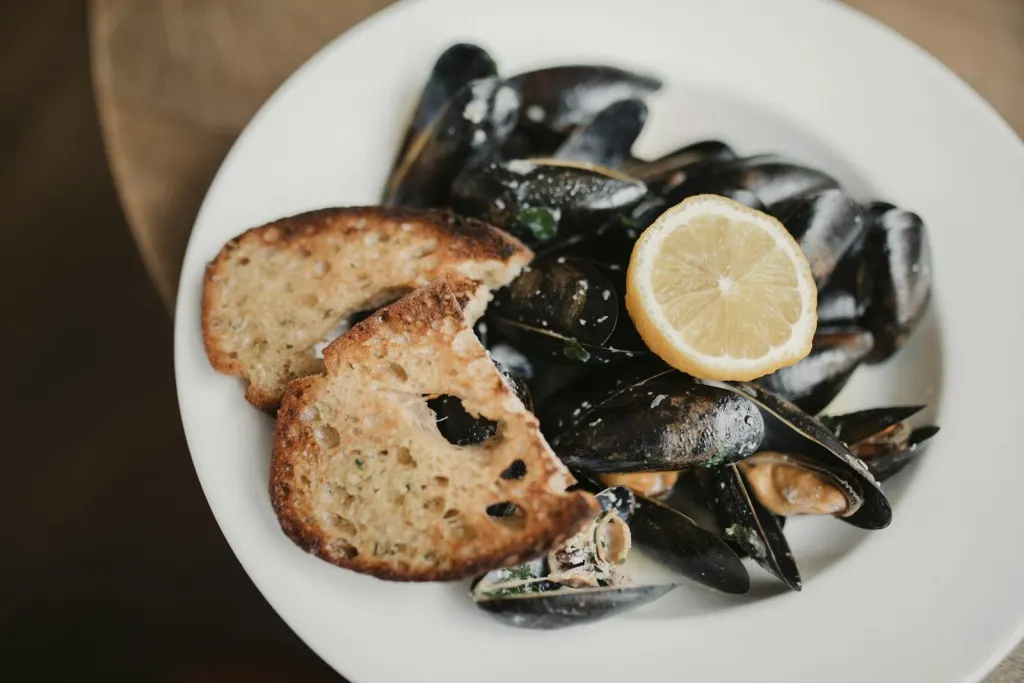 Bowl of mussels with a lemon slice and toasted sourdough