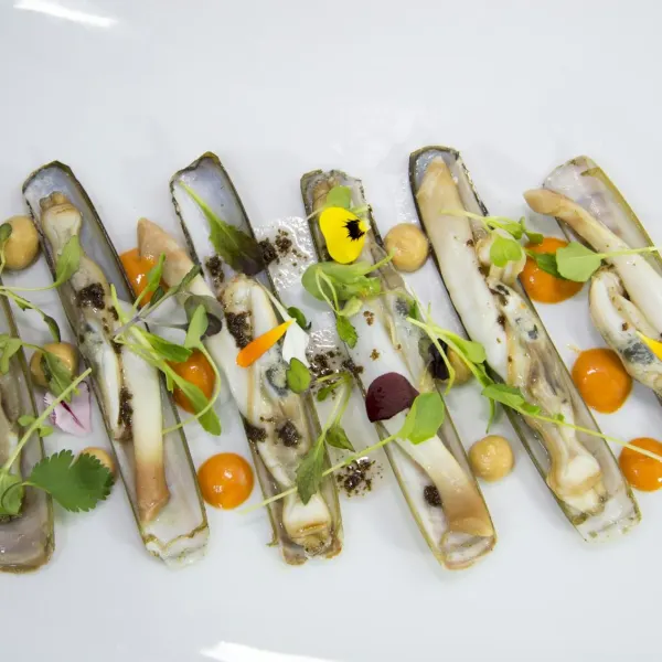 Razor clams dressed with orange sauce and herbs on a white plate