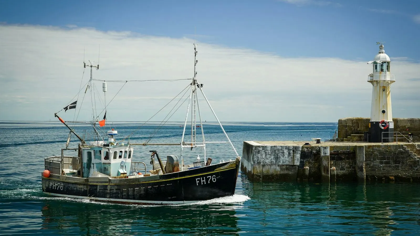A fishing boat heading out past the harbour lighthouse