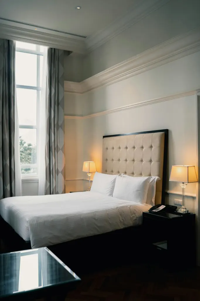 Double bed with a padded headboard and bedside lamps beside tall windows