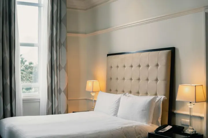 Double bed with a padded headboard and bedside lamps beside tall windows